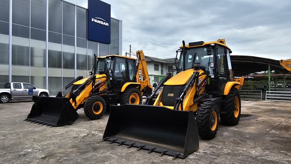 Two yellow JCB backhoe loaders parked in front of a glass-walled building with a blue PANSAR sign