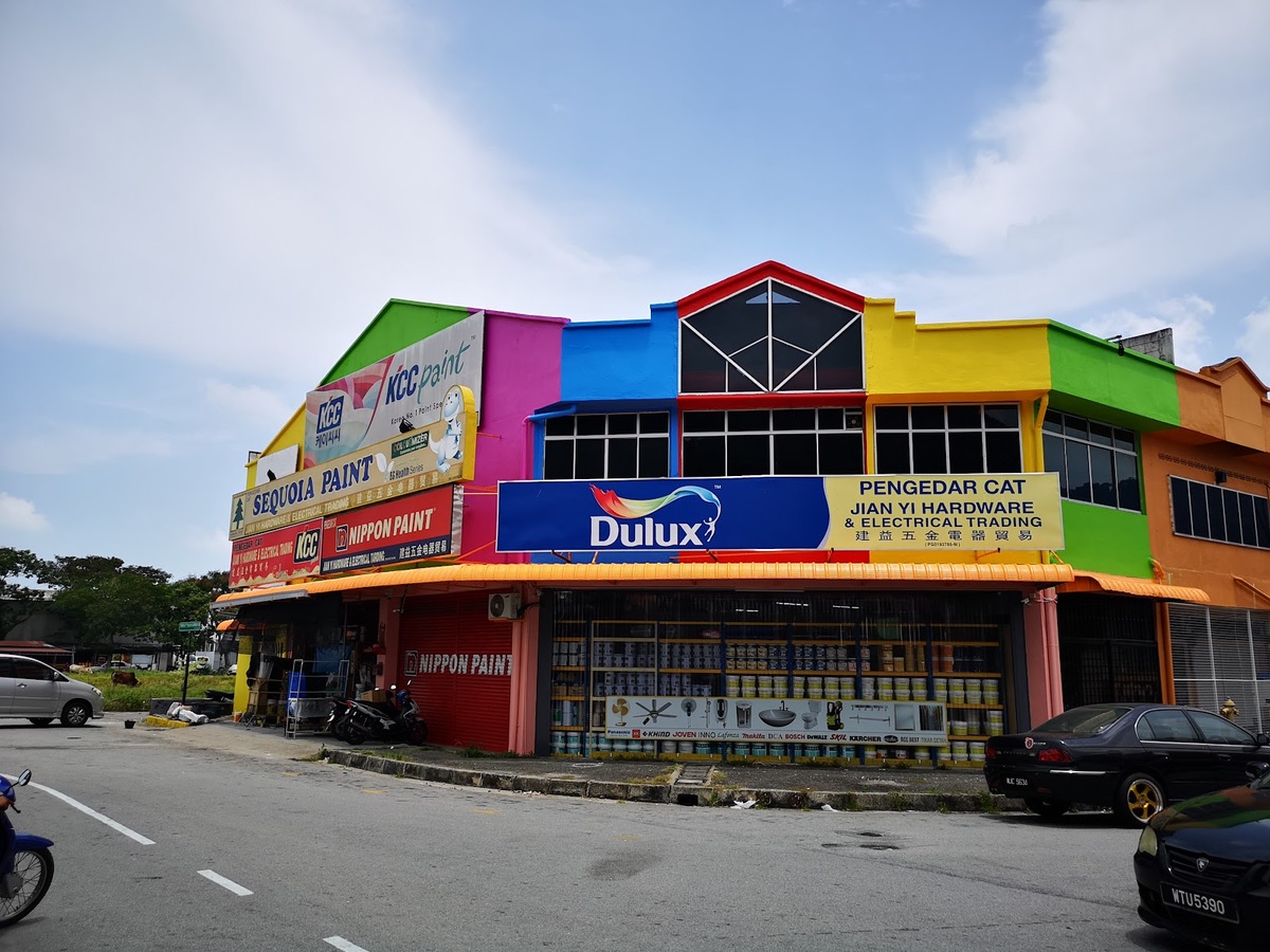 Brightly painted corner shop with paint-brand signboards, an orange awning and shelves of paint tins behind the windows