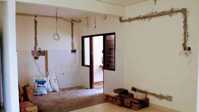 Bare room with fresh grooves cut into the plaster walls for new wiring conduits, sockets boxes exposed and building materials on the floor