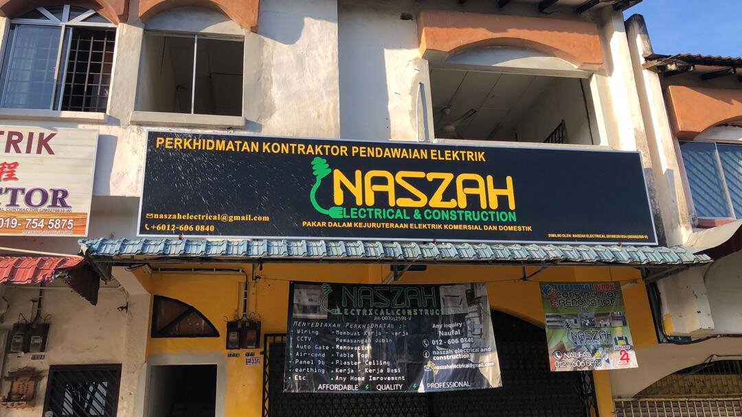 Two-storey shoplot with a black Naszah Electrical & Construction signboard and a banner listing wiring and renovation services over a closed grille