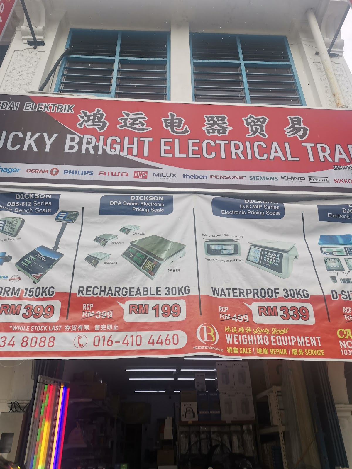 Red signboard reading Lucky Bright Electrical Trading with Chinese characters and a row of brand logos, above a red banner advertising Dickson weighing scales and a shop entrance with coloured LED tubes