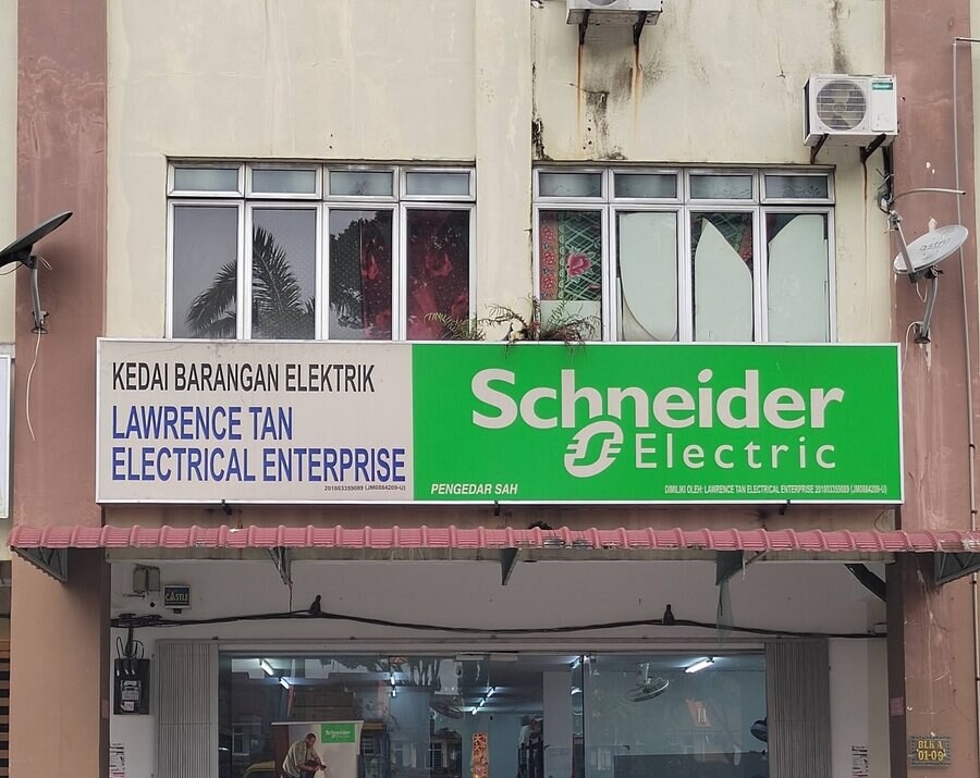 Shop-lot signboard reading Kedai Barangan Elektrik, Lawrence Tan Electrical Enterprise, beside a green Schneider Electric panel, above a glass shopfront with a Blk A 01-09 unit plate