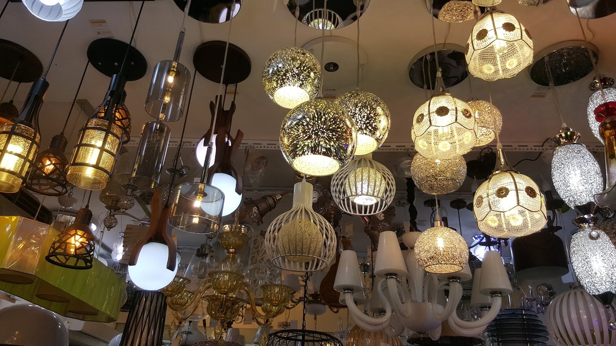 Shop ceiling crowded with lit pendant lamps, glass globes, lanterns and a white chandelier