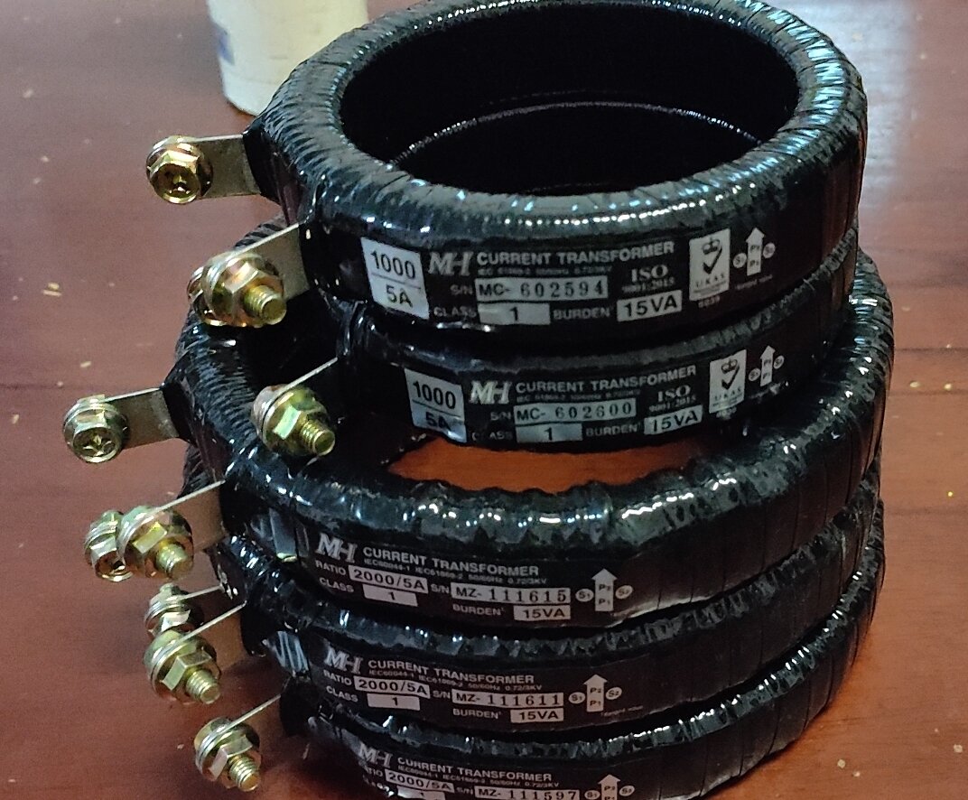 A stack of black ring-shaped current transformers with brass terminals and white rating labels