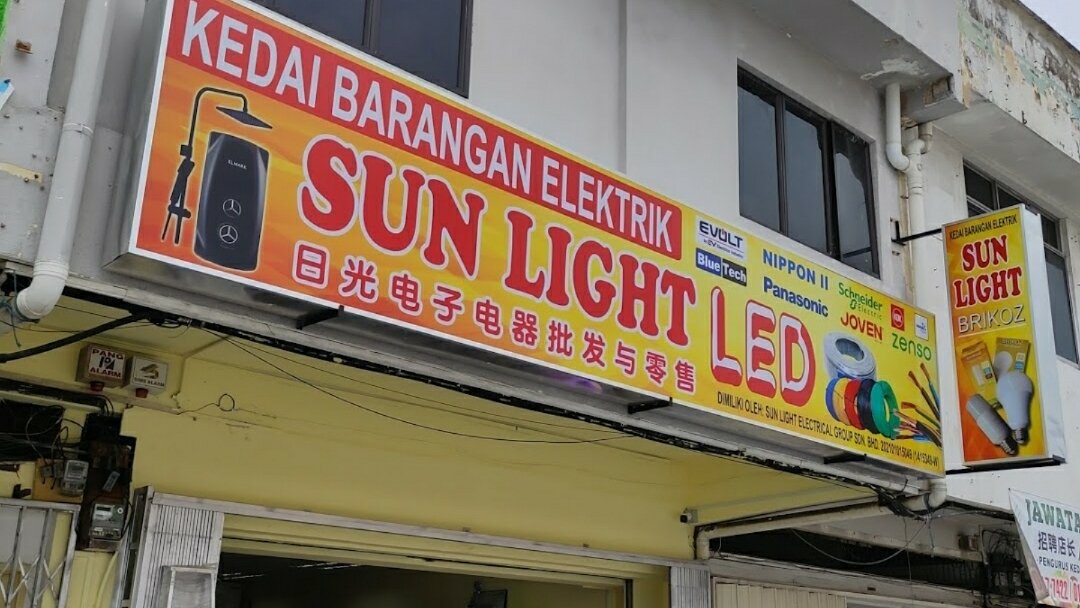 Yellow and orange "Kedai Barangan Elektrik Sun Light LED" signboard with brand logos and pictures of cable coils and LED bulbs