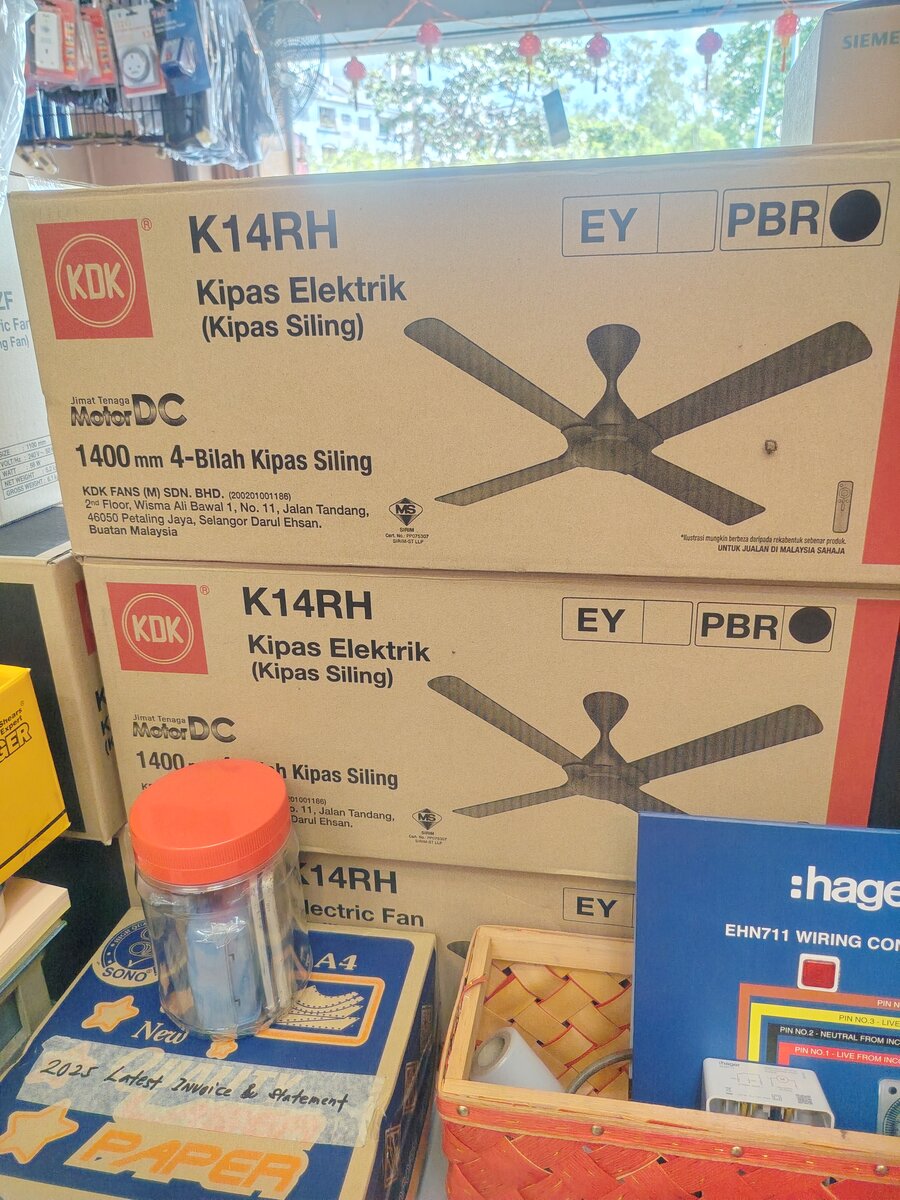 Three brown KDK ceiling-fan cartons stacked on a counter, with a blue Hager wiring-connector display and a jar in the foreground