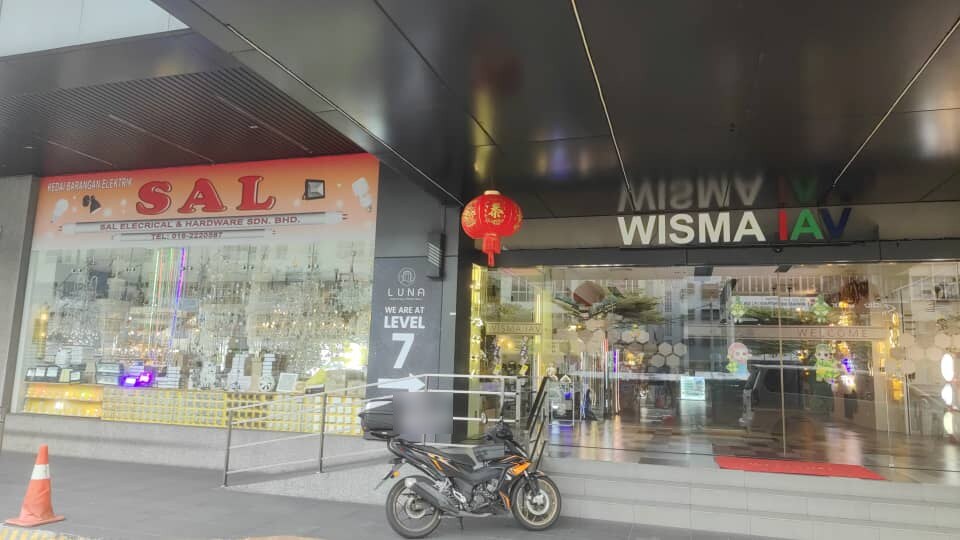 Orange SAL signboard over a glass shopfront full of chandeliers, beside the Wisma IAV entrance, with a motorcycle parked in front