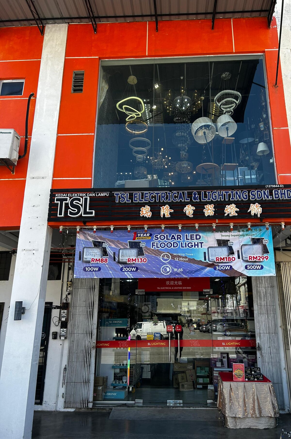Orange shophouse with a black TSL Electrical & Lighting signboard, chandeliers in the upper window and a blue solar LED flood light banner over the glass door