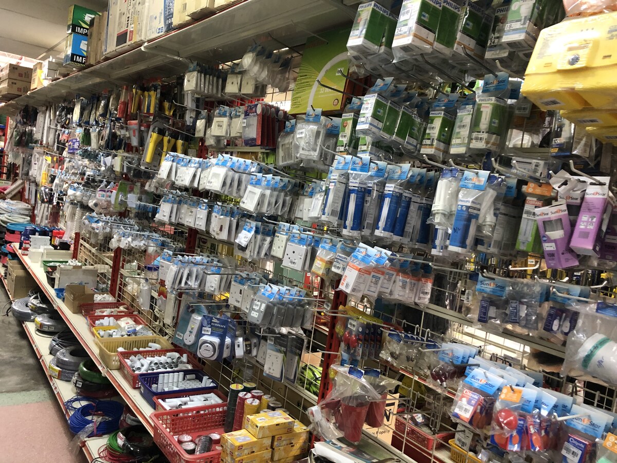 Long shop aisle with pegboards of bagged lamps, switches and sockets, baskets of white conduit fittings and coils of cable on the bottom shelf