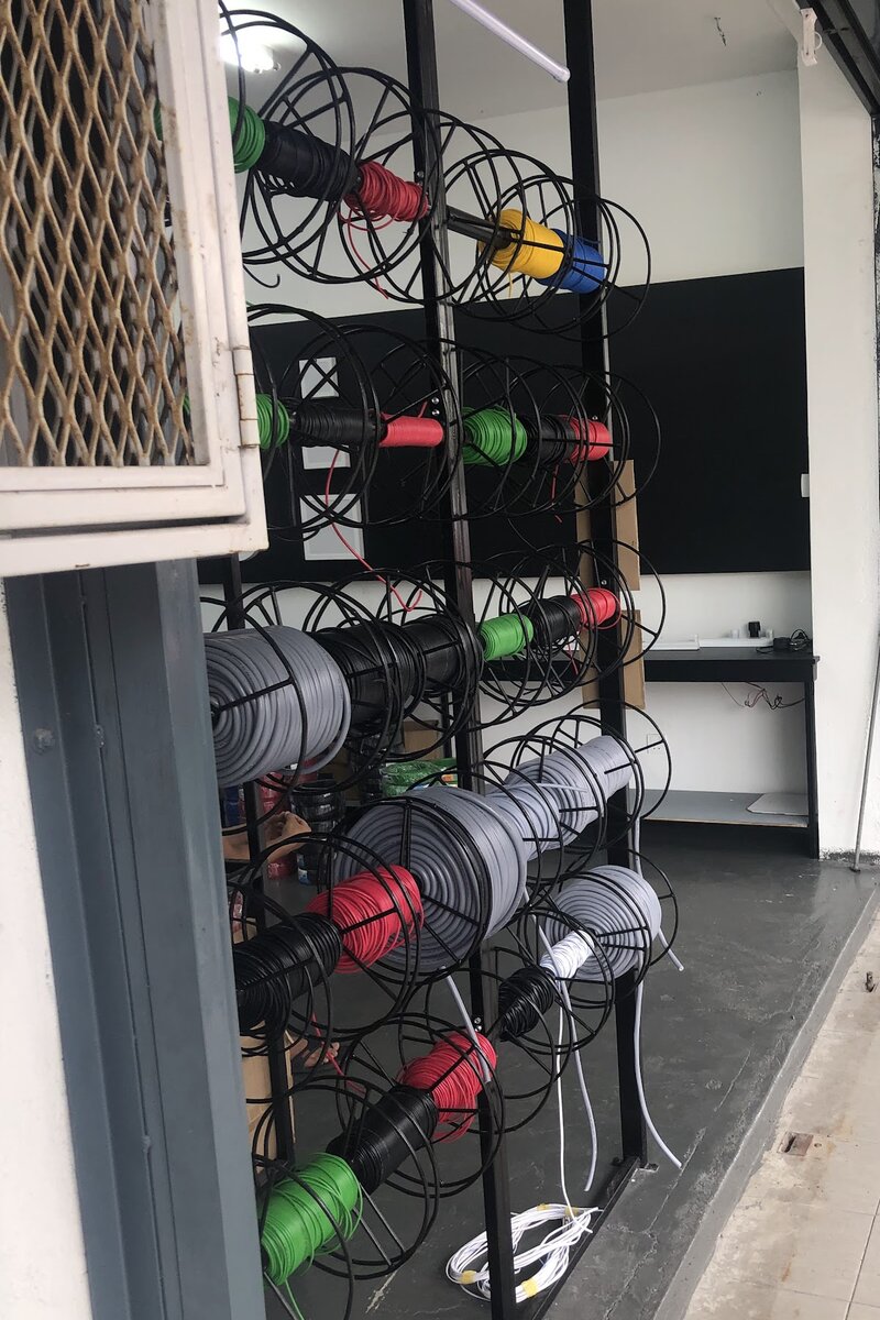 Black metal racks holding reels of red, green, black, yellow, blue and grey cable inside an open shopfront