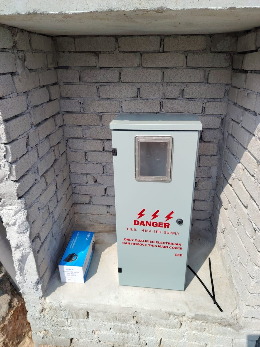 Grey metal meter enclosure with a viewing window and a red DANGER T.N.B. 415V 3PH SUPPLY warning label, standing in a brick recess
