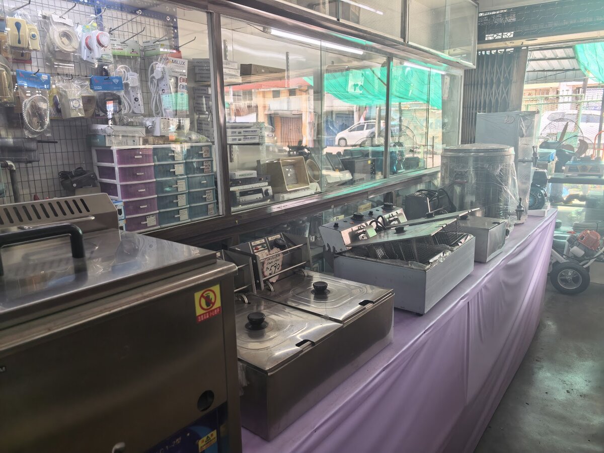 Pegboard of packaged extension sockets and plugs next to glass cabinets and a row of stainless-steel deep fryers