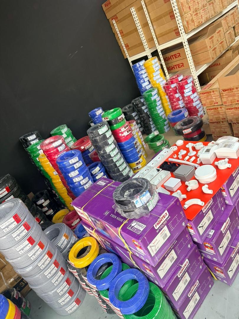 Floor stacked with coloured wire coils, purple ceiling fan cartons and a red board of white conduit fittings