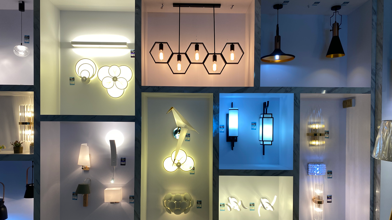 Wall of illuminated display niches with wall lamps and hexagonal pendant lights