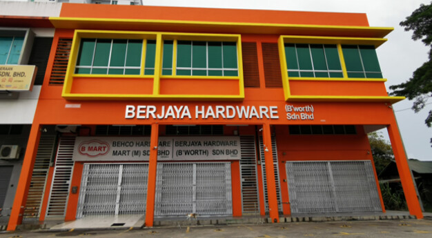 Orange two-storey shop building with the sign Berjaya Hardware B'worth Sdn Bhd and, over the shutters, Behco Hardware Mart and B Mart signs