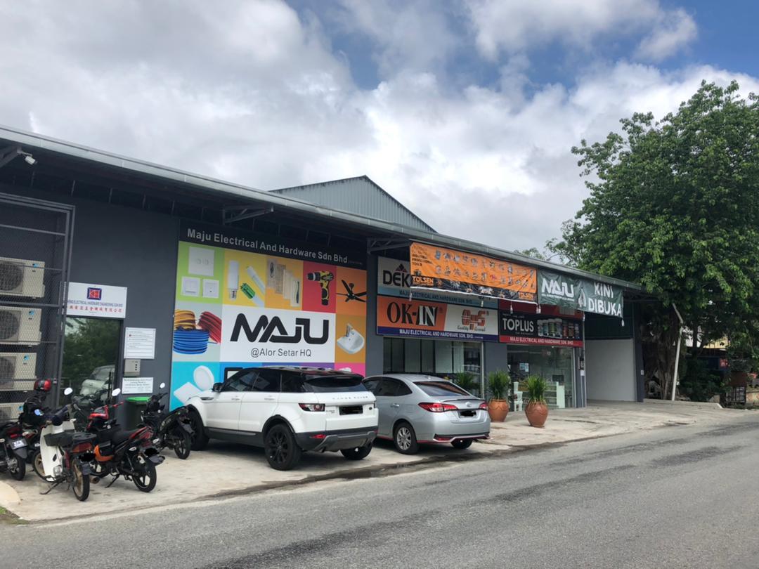 Grey single-storey shop with a colourful MAJU @Alor Setar HQ signboard, brand banners above the glass front and cars parked outside