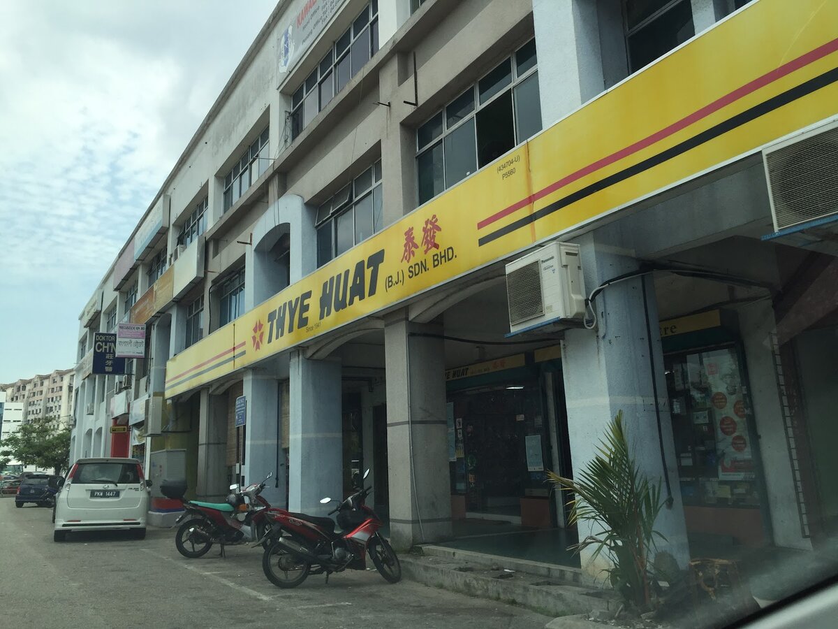 Long yellow Thye Huat (B.J.) Sdn Bhd signboard running along the ground floor of a four-storey shop block, with motorcycles parked in front