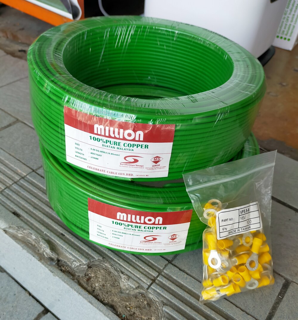 Two green coils of electrical cable with red and white labels and a small bag of yellow ring terminals on a tiled floor