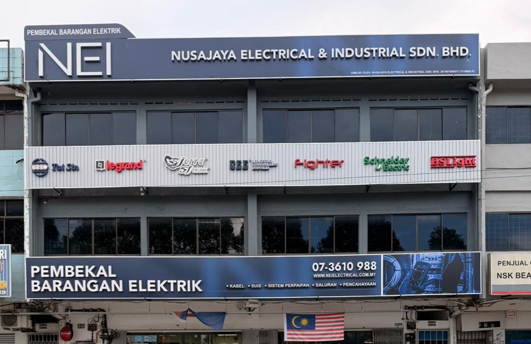 Three-storey shophouse with a navy NEI Nusajaya Electrical & Industrial signboard, a white strip of brand logos and a lower Pembekal Barangan Elektrik banner