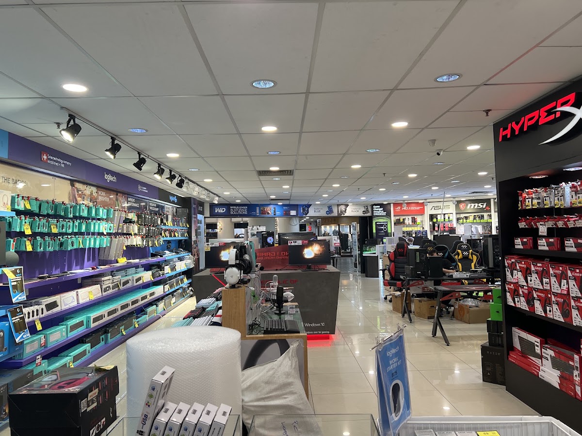 Computer store floor with a Logitech accessories wall, a HyperX display and gaming chairs