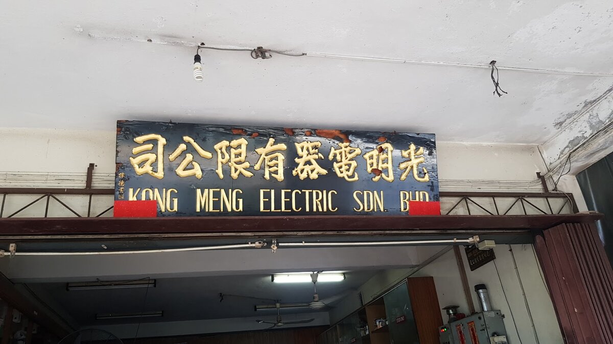 Black wooden signboard with gold Chinese characters and the words Kong Meng Electric Sdn Bhd above an open shop entrance