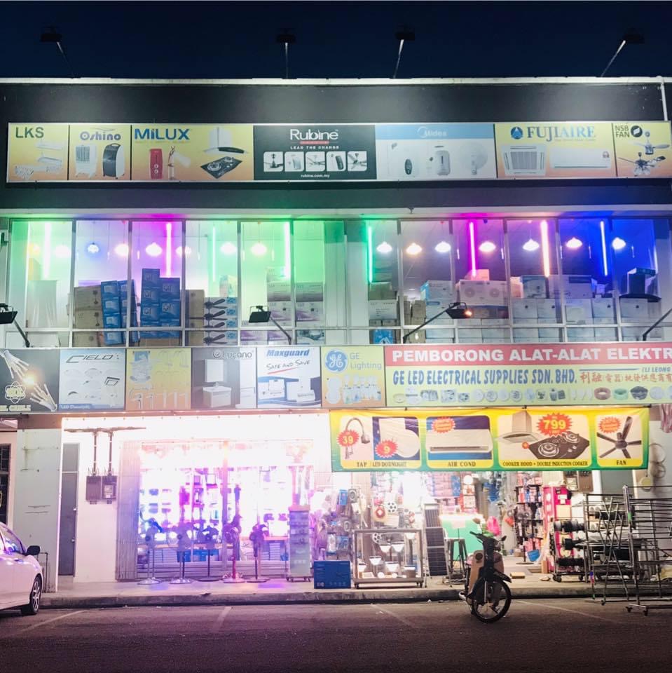 Two-storey shop lit in green, pink and blue with brand panels and a red Pemborong Alat-Alat Elektrik signboard