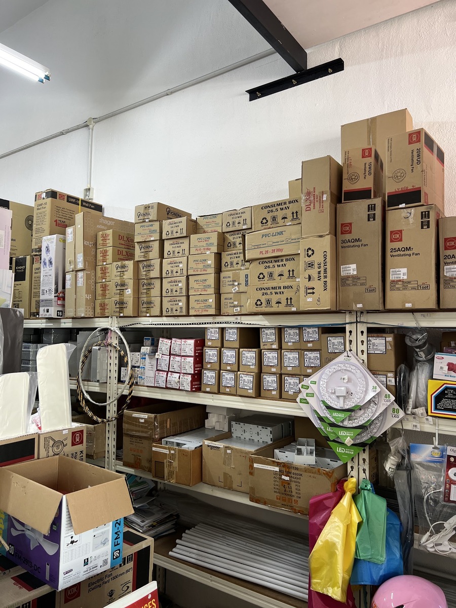 Metal shelving stacked with consumer box cartons, red isolator boxes, contactor boxes, KDK fan cartons and a hanging rack of LED ceiling modules