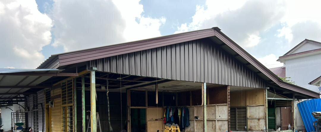 Long single-storey building with a sloping brown metal roof and open timber-framed walls, partly stripped for renovation, under a cloudy sky