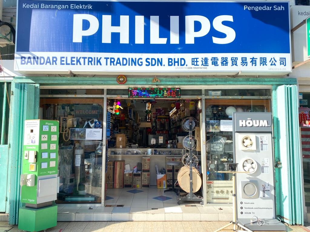 Small electrical shop with a blue Philips signboard reading Bandar Elektrik Trading Sdn Bhd, a green Schneider switch display stand and a fan display stand at the open glass front