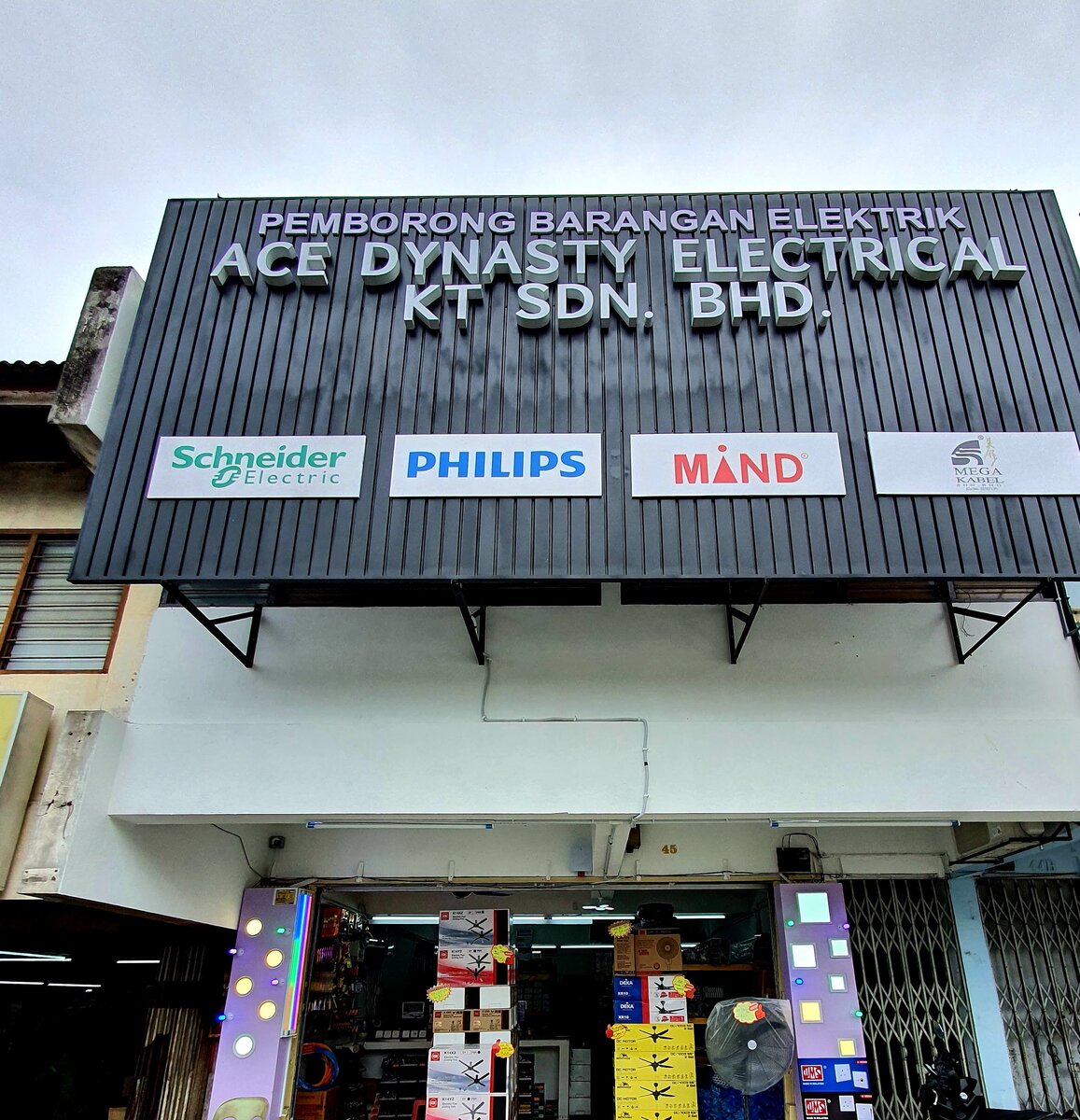 Shophouse with a black signboard reading Ace Dynasty Electrical KT Sdn Bhd and brand panels, open shutter with stacked fan boxes