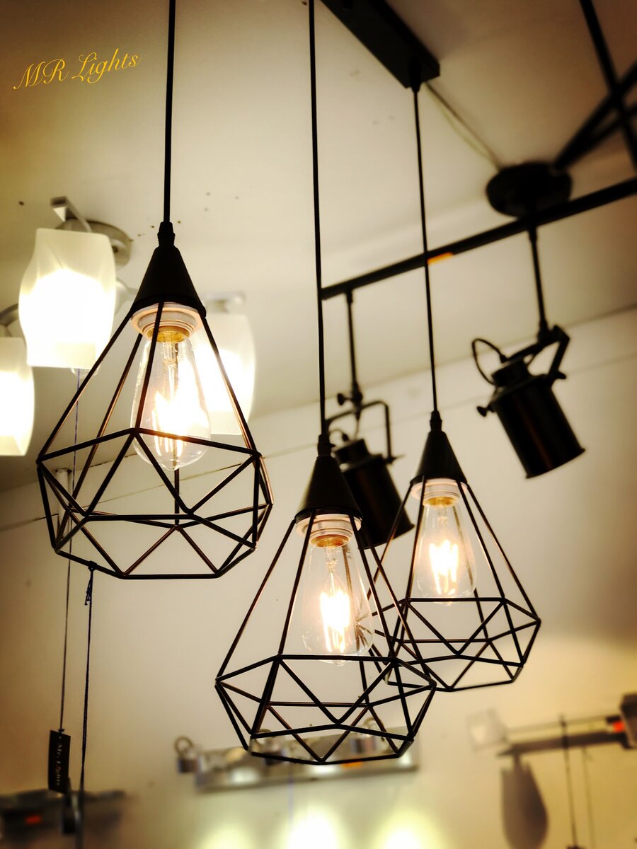 Three black geometric wire-cage pendant lamps with filament bulbs hanging in a lighting showroom