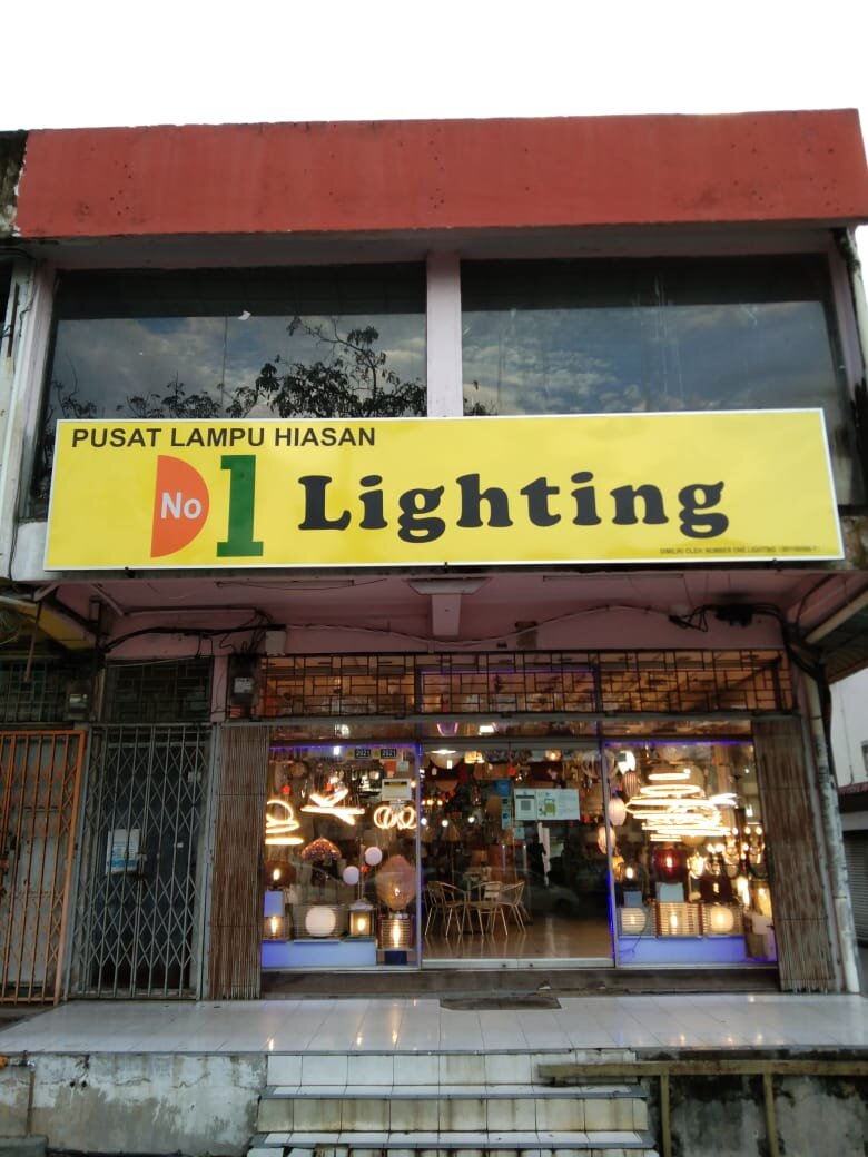 Shophouse with a yellow "Pusat Lampu Hiasan No 1 Lighting" signboard and a lit window full of chandeliers