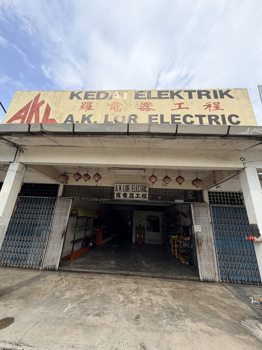 Old shophouse with a yellow Kedai Elektrik A.K. Lor Electric signboard above open folding gates