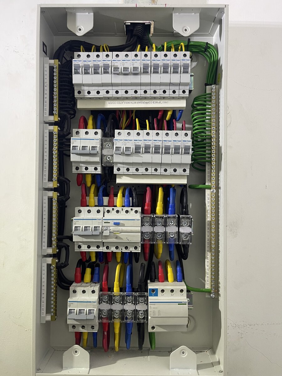 Open grey three-phase distribution board with neatly dressed red, yellow, blue and green cables, rows of miniature circuit breakers and terminal bars