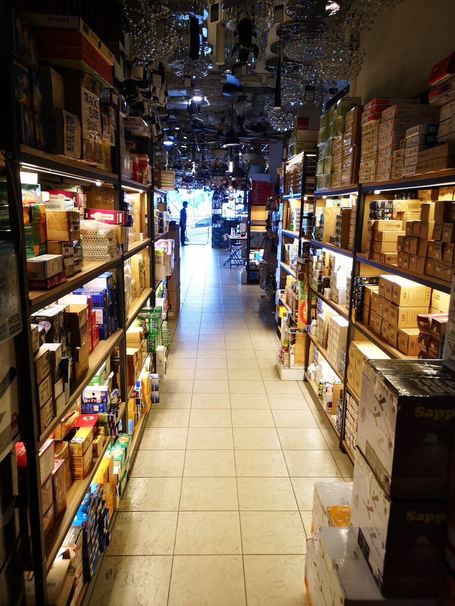 Long shop aisle lined with lit shelves of boxed lamps under rows of hanging lights