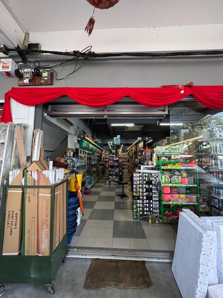 Shop entrance under a red cloth drape, a trolley of LED tube cartons on the left and shelved aisles with a grass-trimmer display inside