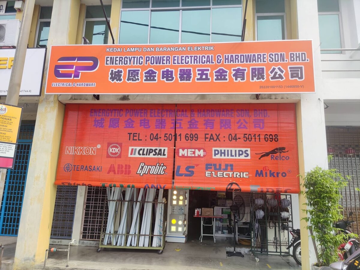 Orange shop sign and shutter printed with brand logos such as Philips, ABB, KDK and Clipsal over a shop front with trunking and lit LED panels