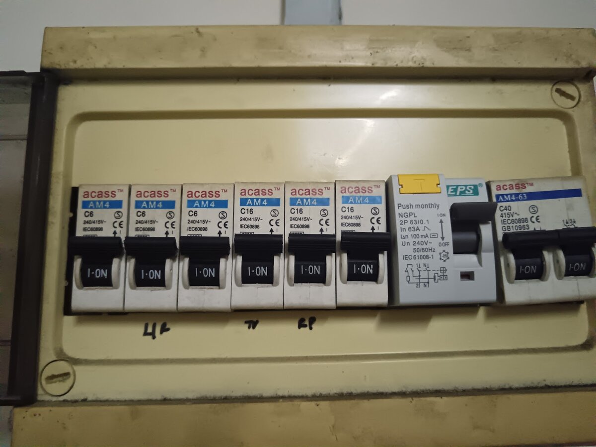 Cream plastic distribution board with six small Acass breakers, a grey EPS residual current breaker with a yellow test button and a two-pole main breaker, handwritten circuit labels underneath