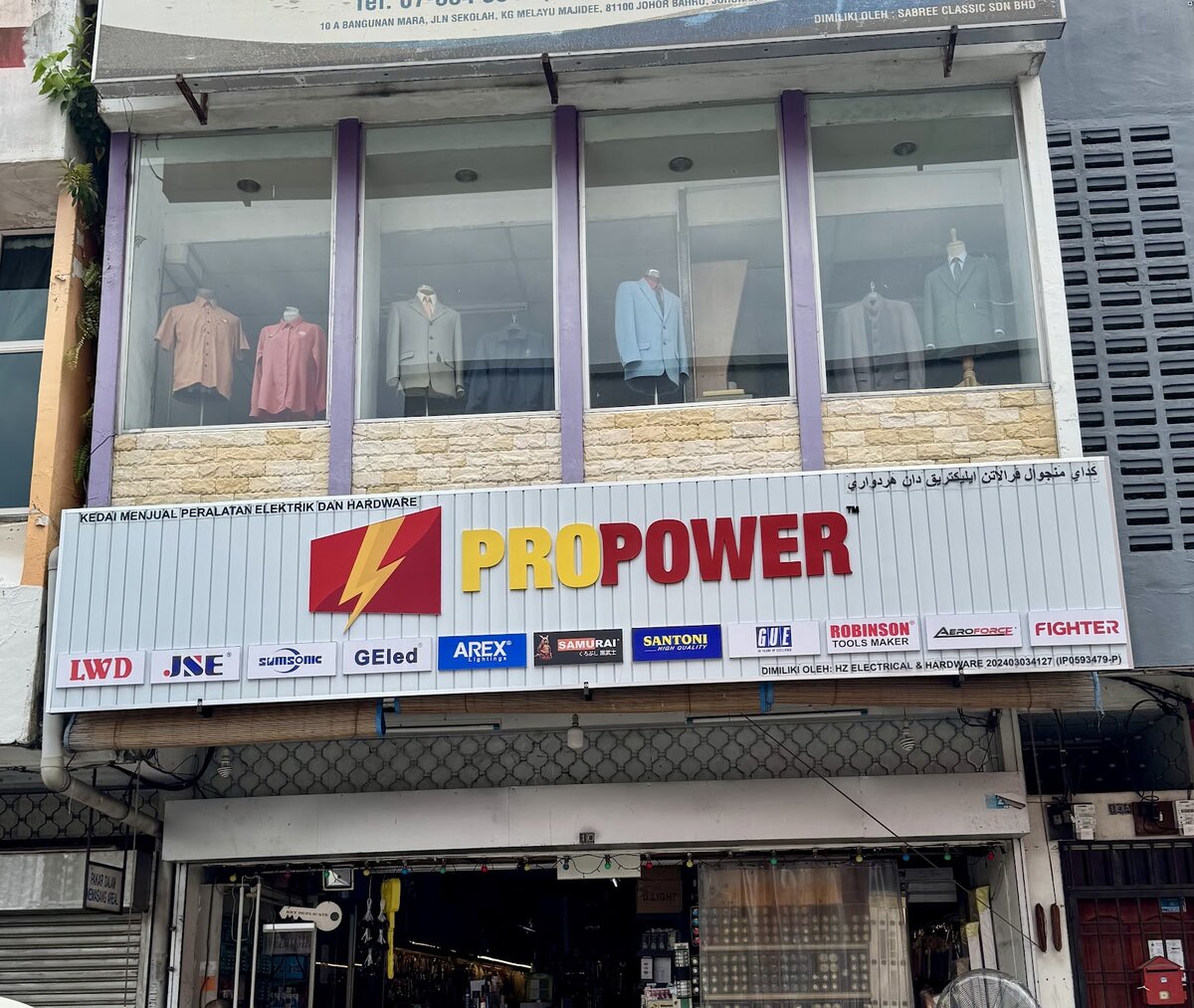 Shop signboard reading Propower, Kedai Menjual Peralatan Elektrik dan Hardware, with a row of brand logos, below a tailor's shop window