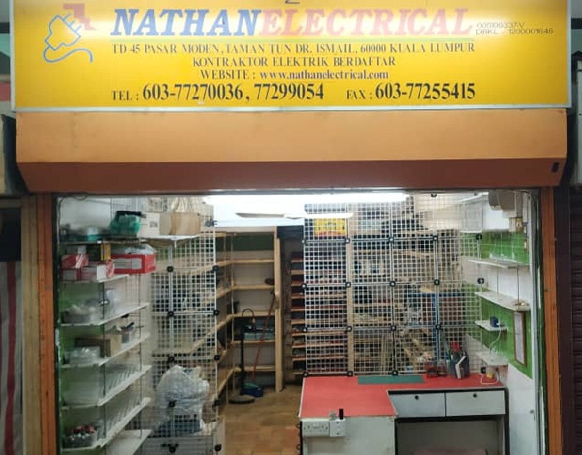 Small market shop unit with a yellow signboard reading Nathan Electrical, TD 45 Pasar Moden Taman Tun Dr Ismail, Kontraktor Elektrik Berdaftar, with shelves and a red-topped counter inside