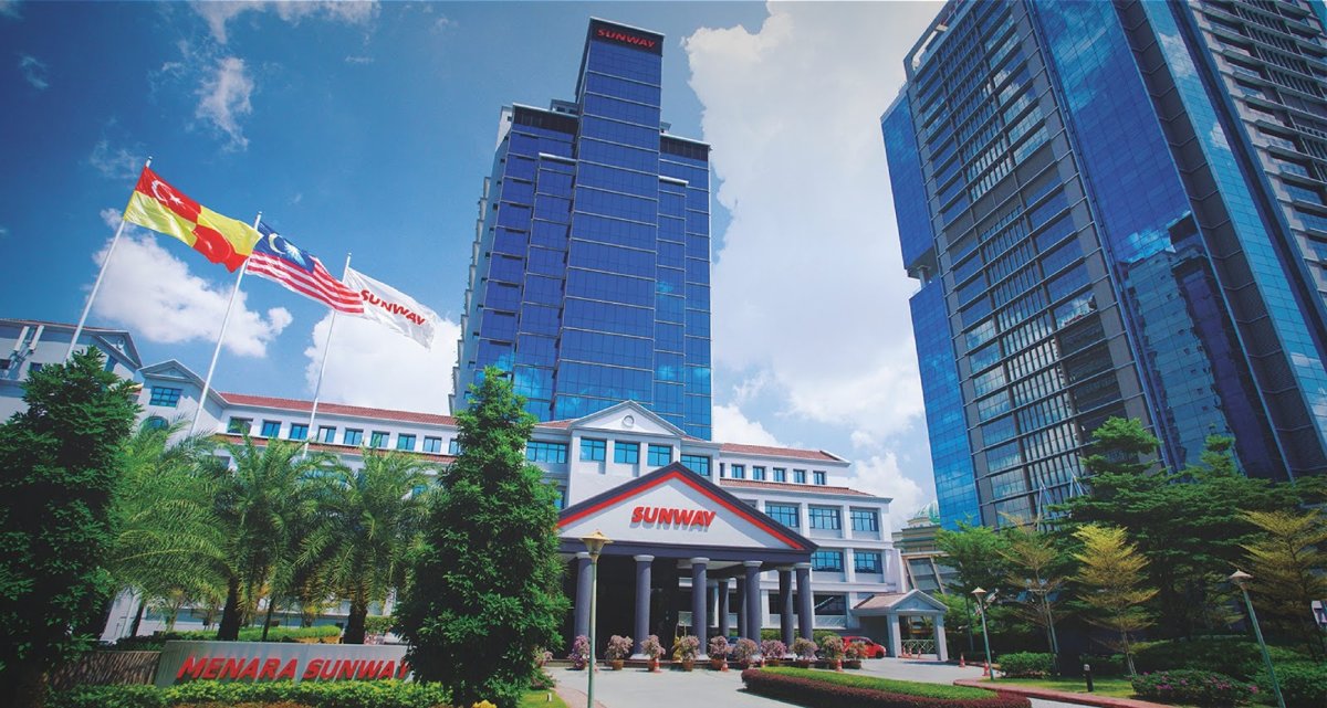 Glass office towers behind a low white building with a red Sunway sign, flags and landscaped gardens, with Menara Sunway lettering in the foreground