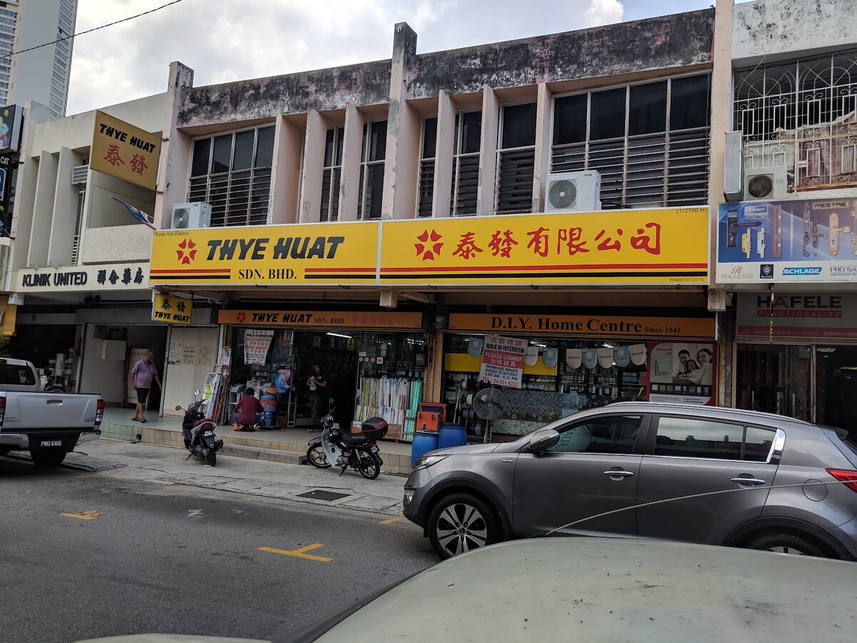Two-storey shophouse with a yellow Thye Huat Sdn Bhd signboard in English and Chinese above an open shopfront, cars parked on the street