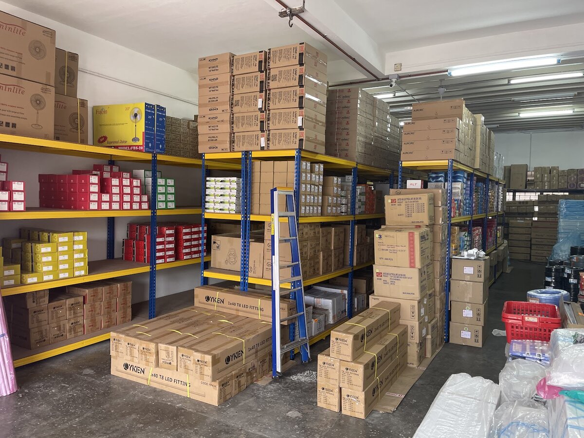 Warehouse aisles with yellow and blue racking full of cartons, boxed fans on the top shelves and pallets of LED fitting boxes on the floor