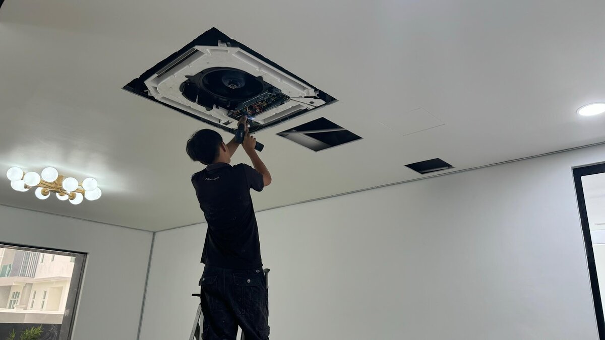 Technician on a ladder working on an open ceiling cassette air-conditioner