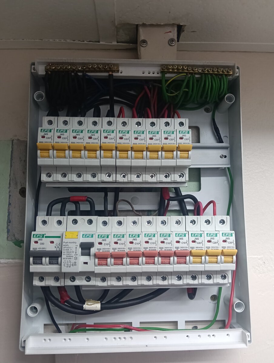 Open grey distribution board with a top row of ten yellow-handled EPS breakers and a bottom row with a two-pole main switch, an RCCB and red and yellow breakers, neutral and earth bars along the top