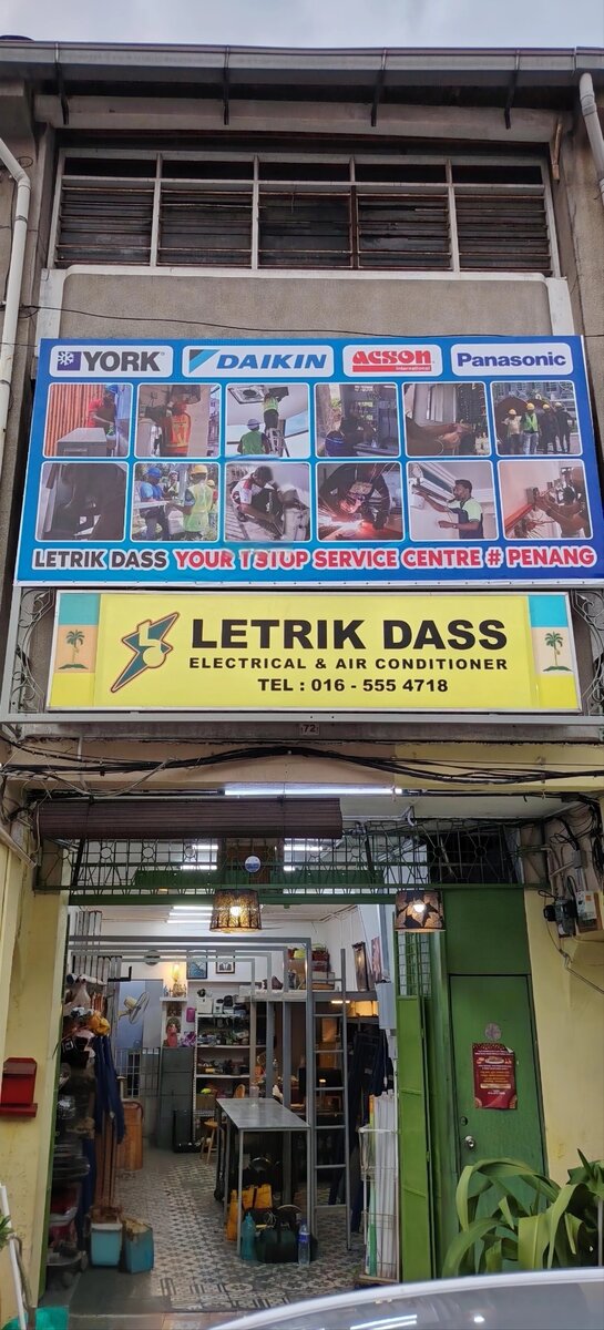 Shophouse front with a blue banner of York, Daikin, Acson and Panasonic logos above a yellow Letrik Dass Electrical & Air Conditioner signboard showing 016-555 4718, and an open workshop below