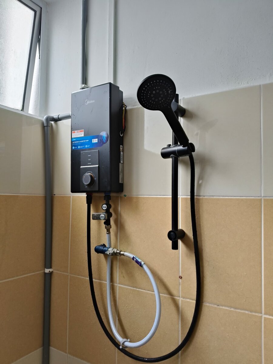 Black instant water heater with a hand shower and rail mounted on a beige-tiled bathroom wall, with grey conduit running down from the ceiling