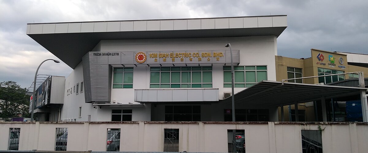 White two-storey office block with a slatted sign reading Kim Siah Electric Co. Sdn. Bhd. in gold letters beside a red and gold KS logo, behind a boundary wall
