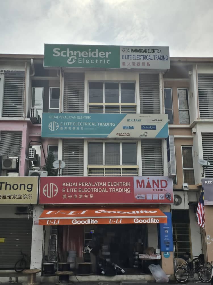 Three-storey shophouse with a green Schneider Electric and E Lite Electrical Trading signboard at the top, a blue distributor sign and a red Mind Electrical shop sign over an orange Goodlite awning
