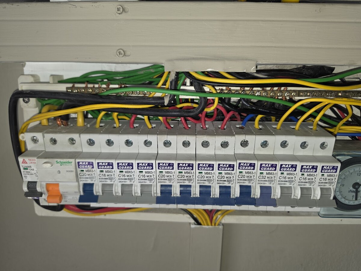 Open distribution board with a main switch, a Schneider residual-current breaker and a row of thirteen Maxguard miniature circuit breakers, with a time switch at the right